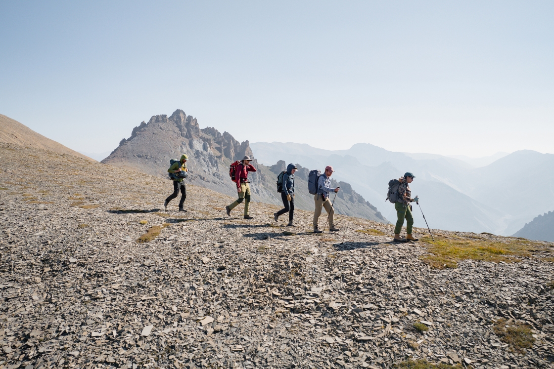 Researchers hike down from the reef with backpacks full of rock/fossil samples.