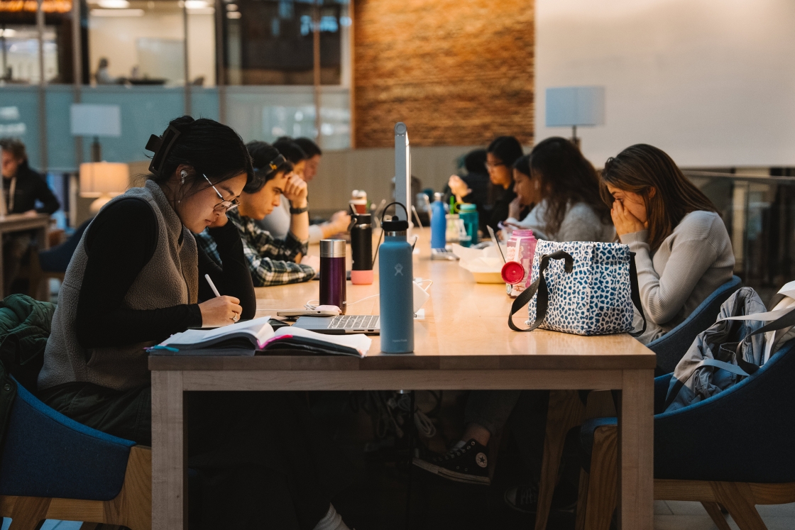 Students sit at a desk facing each other and studying