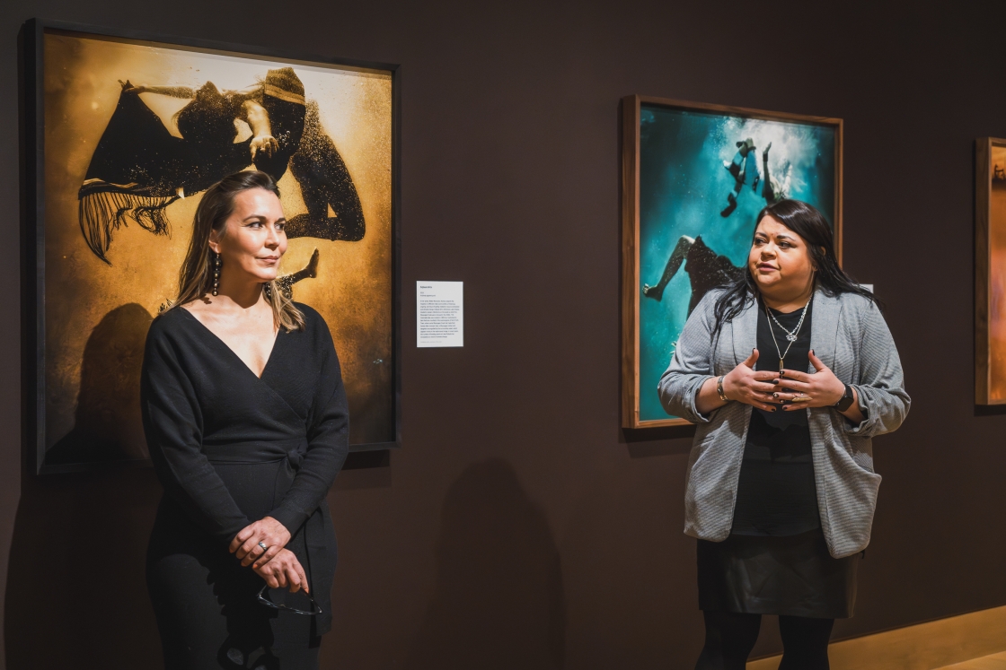 Cara Romero and Jami Powell stand in front of photos and discuss the exhibit