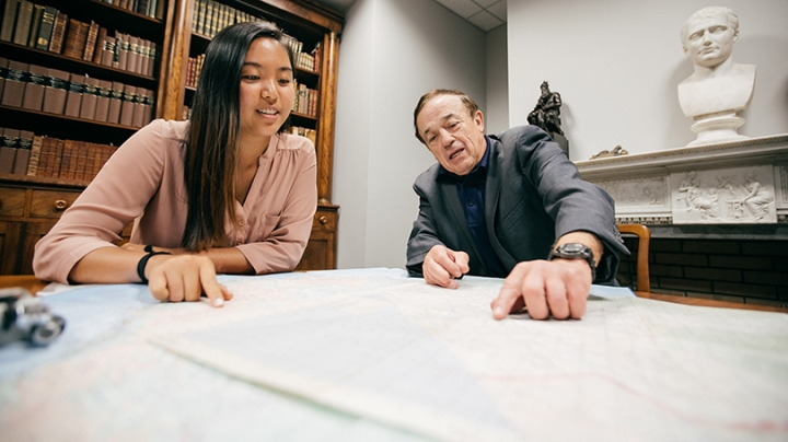 a student and professor examining a map spread out on a table