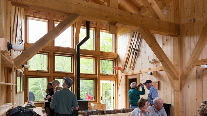 the pale wood interior of the Class of 1967 bunkhouse, with people inside taking photos and sitting at a table